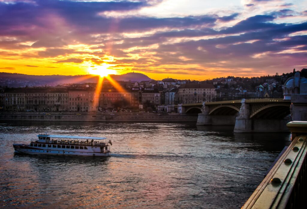 Scenic sunset over Budapest featuring the iconic Margaret Bridge and river cruise boat.